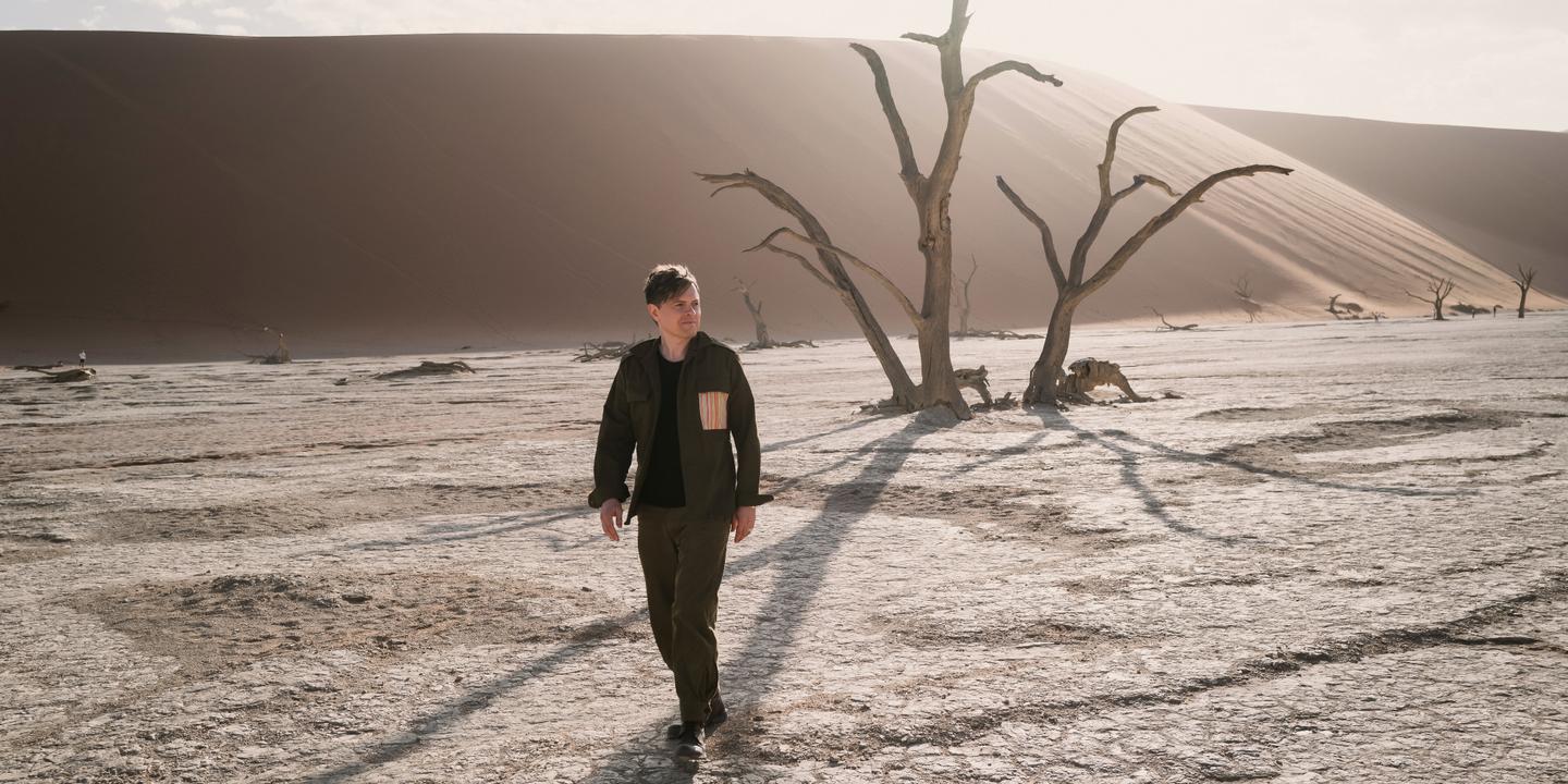 Michael Patrick Kelly läuft zwischen abgestorbenen Kameldornbäumen und hohen Sanddünen durch das Deadvlei in Namibia