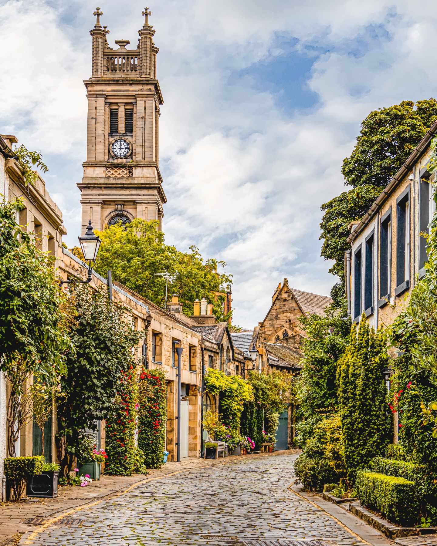 Kopfsteinpflasterstraße in Edinburgh mit begrünten Sandsteingebäuden und historischem Kirchturm im Hintergrund
