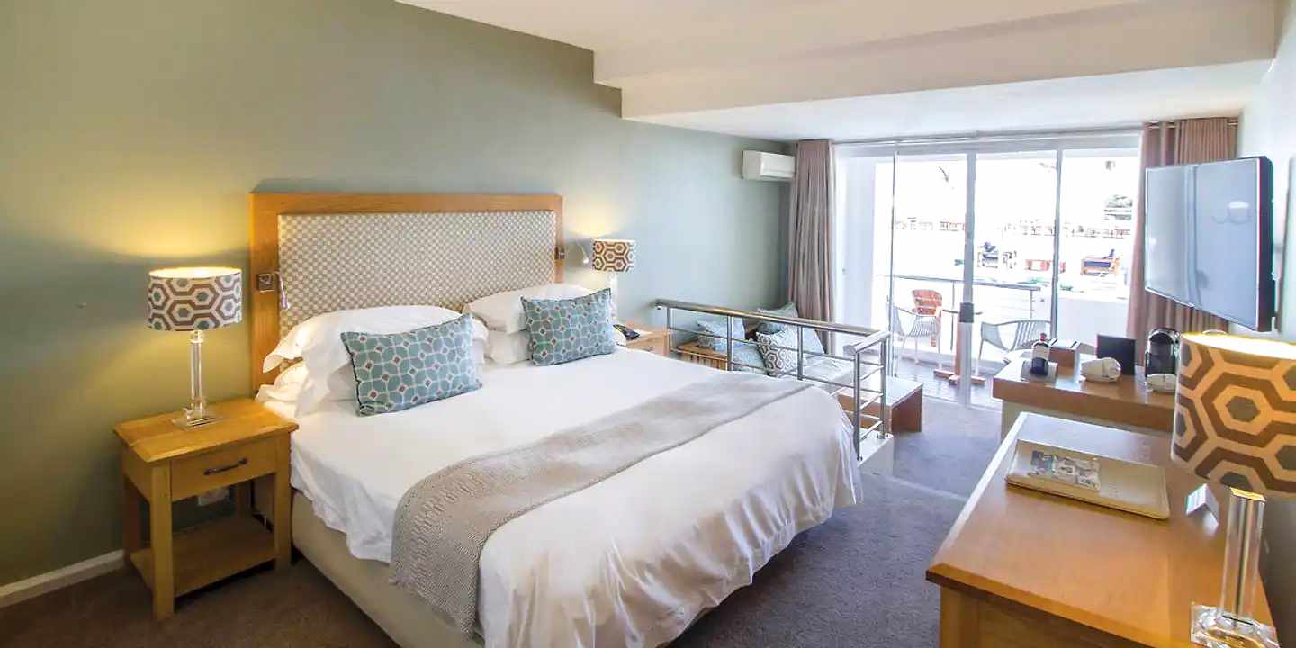 Modernes Zimmer im The Bay Hotel Kapstadt mit Balkon, Doppelbett, stilvollen Lampen und Blick auf die Poolterrasse
