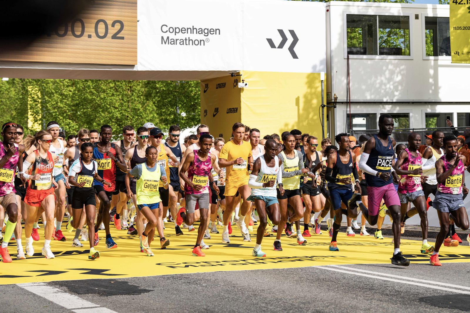 Marathon-Läufer bunt gekleidet starten beim Kopenhagen-Marathon den Lauf und laufen unter einem Torbogen mit Zeitanzeigee durch.