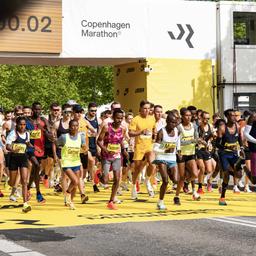 Marathon-Läufer bunt gekleidet starten beim Kopenhagen-Marathon den Lauf und laufen unter einem Torbogen mit Zeitanzeigee durch.