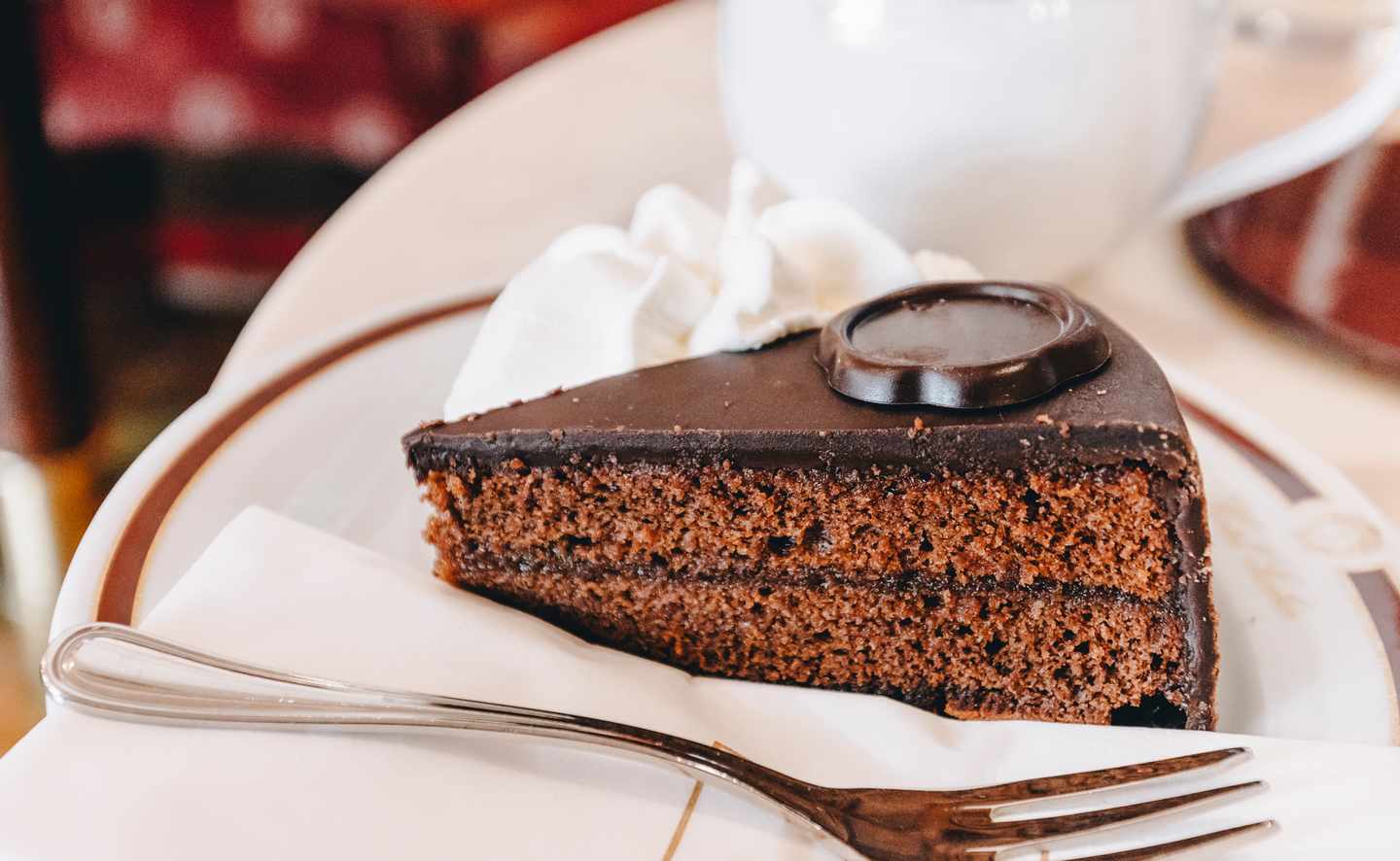 Stück Sachertorte mit Schokoladenglasur und Schlagsahne auf einem weißen Teller in einem Wiener Café