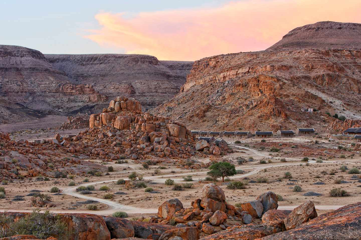 Felsige Berglandschaft mit verstreuten Büschen und kleinen Gebäuden nahe dem Fish River Canyon in Namibia