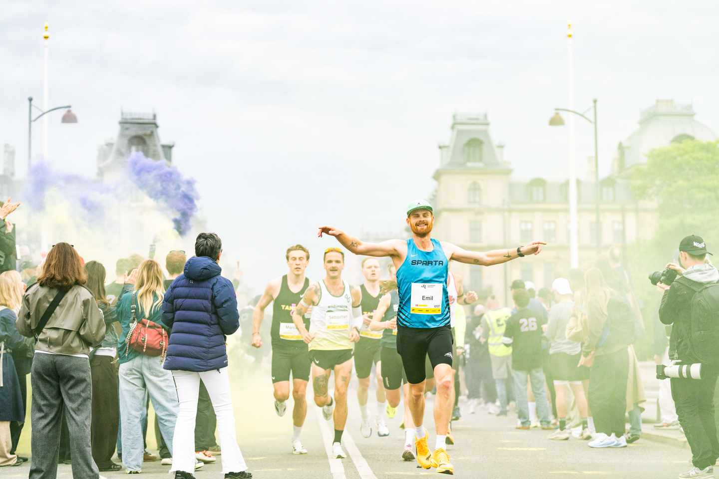 55261216140_25035b9ac2_o.jpg Läufer mit blauem Shirt breitet die Arme aus beim Kopenhagen-Marathon und im Hintergrund sind blauer Nebel und Publikum.