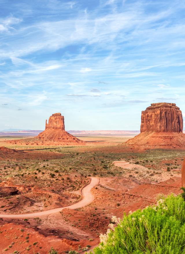 Rundreisen Nordamerika Landschaft mit roten Felsformationen und einem gewundenen Weg unter blauem Himmel mit Wolken