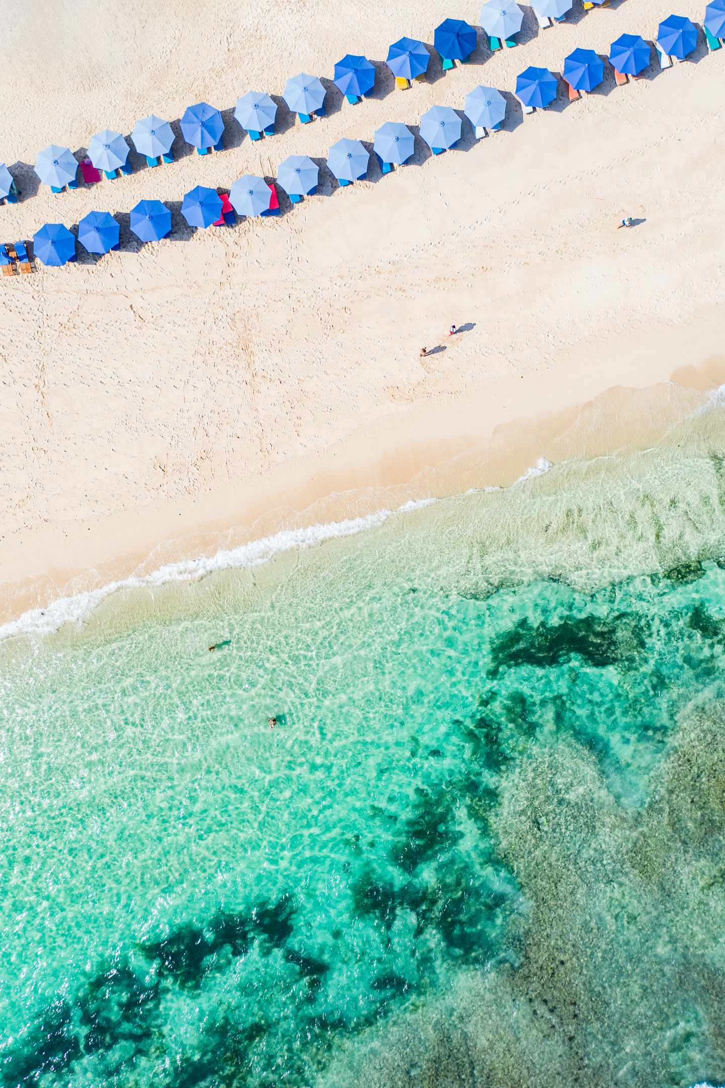 GettyImages-2132213436.jpg Der Melasti-Strand mit klarem türkisfarbenem Wasser das auf den Sandstrand trifft an dem bunte Sonnenschirme in Reihen angeordnet sind
