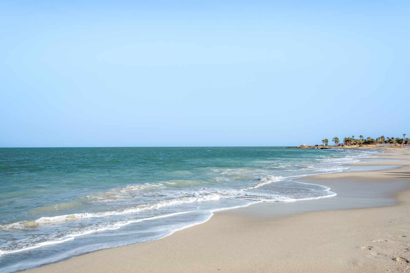 Sanft geschwungener Sandstrand mit türkisfarbenem Meer und klarem Himmel an der Küste von Djerba in Tunesien