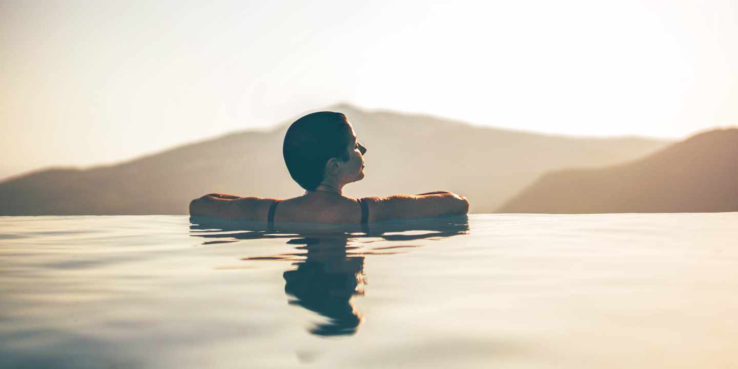 wellnessurlaub-infinity-pool-sonnenuntergang-berge-frau-entspannung-panorama-g-2159812691.jpg