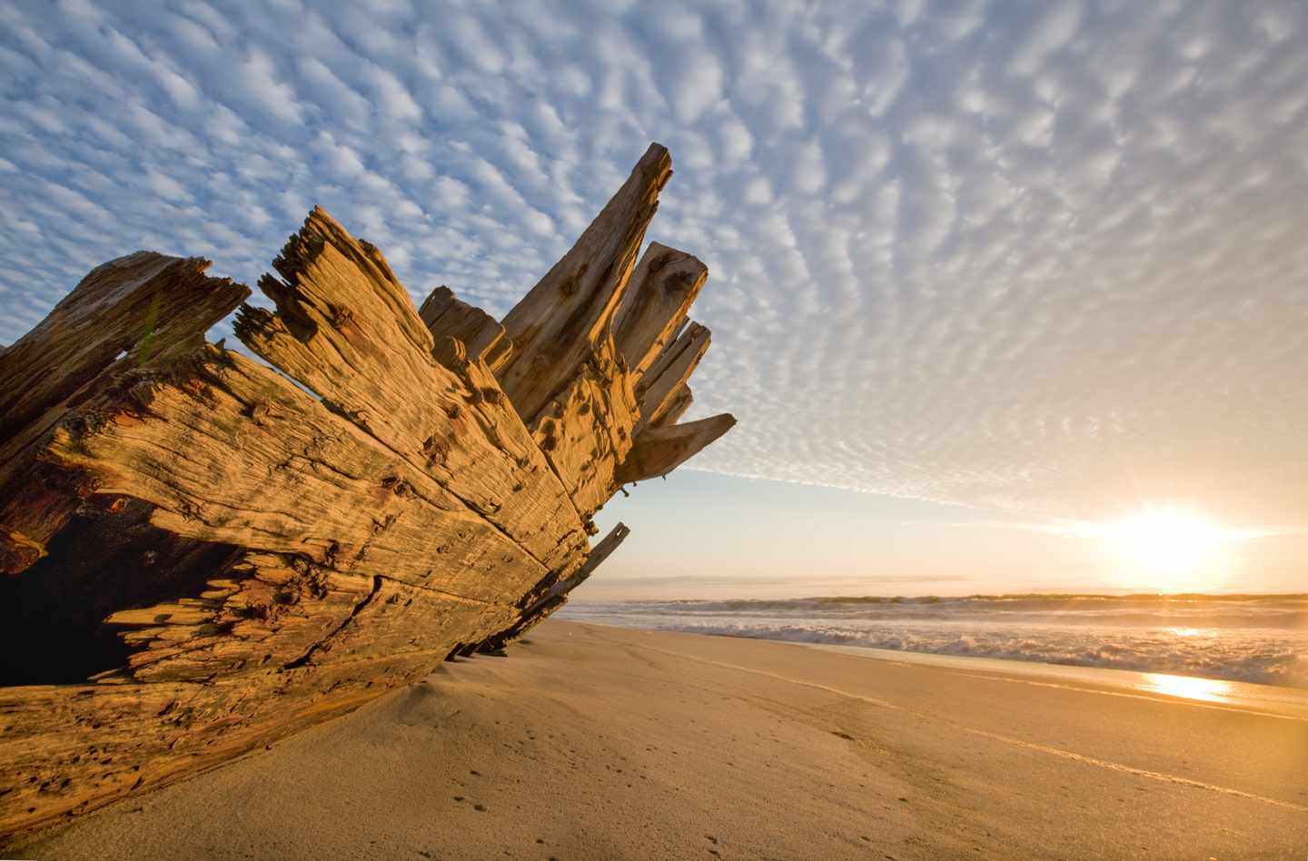 Verwittertes Schiffswrack am Sandstrand der Skeleton Coast in Namibia bei tief stehender Sonne und auflaufenden Wellen