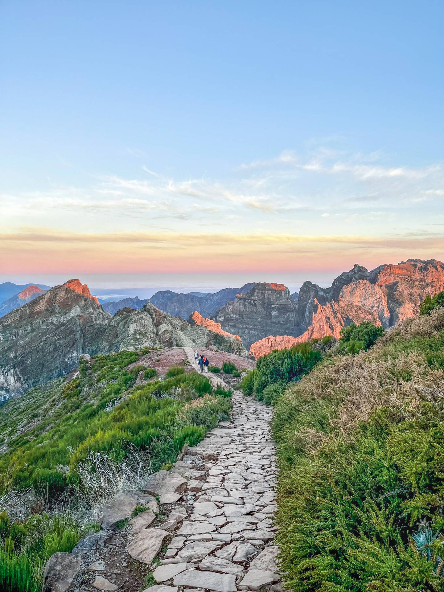 Steinweg mit Wandernden am Pico do Arieiro vor schroffen Berggipfeln im Morgenlicht auf Madeira, Portugal