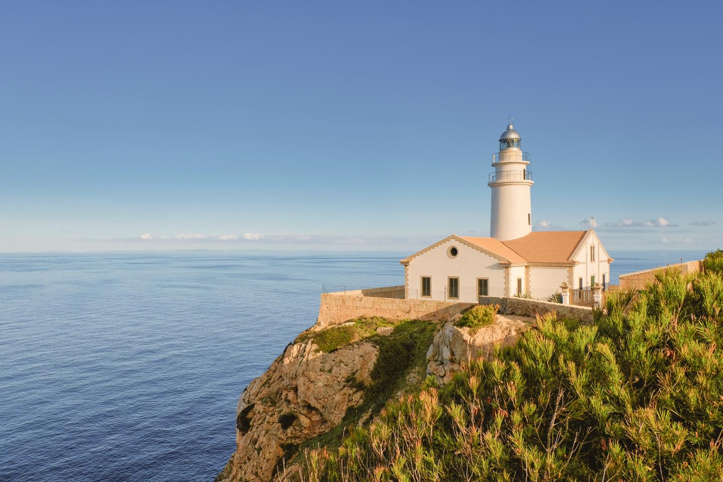 Weißer Leuchtturm mit Wächterhäuschen vor blauem Meer