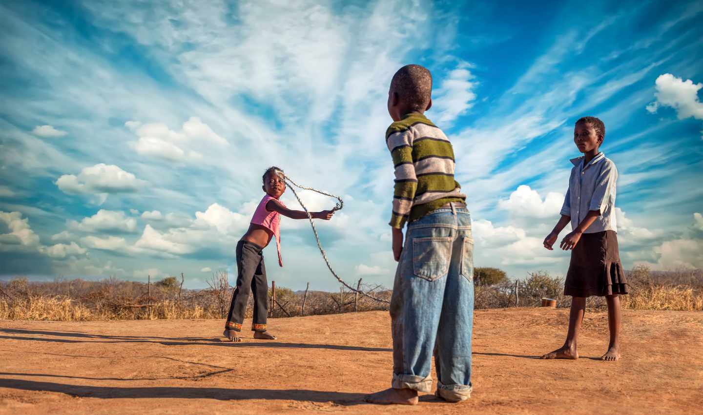 Drei Kinder spielen beim Seilspringen gemeinsam auf einem Platz in einem Dorf in Botswana