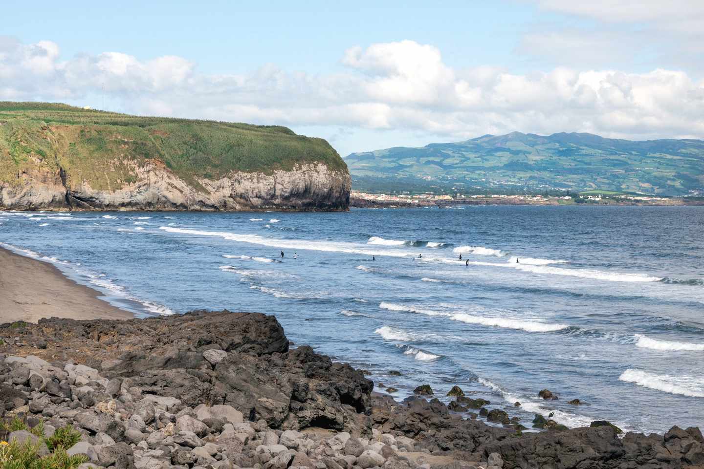 Surfer am schwarzen Sandstrand Praia de Santa Bárbara auf São Miguel vor steiler Steilküste
