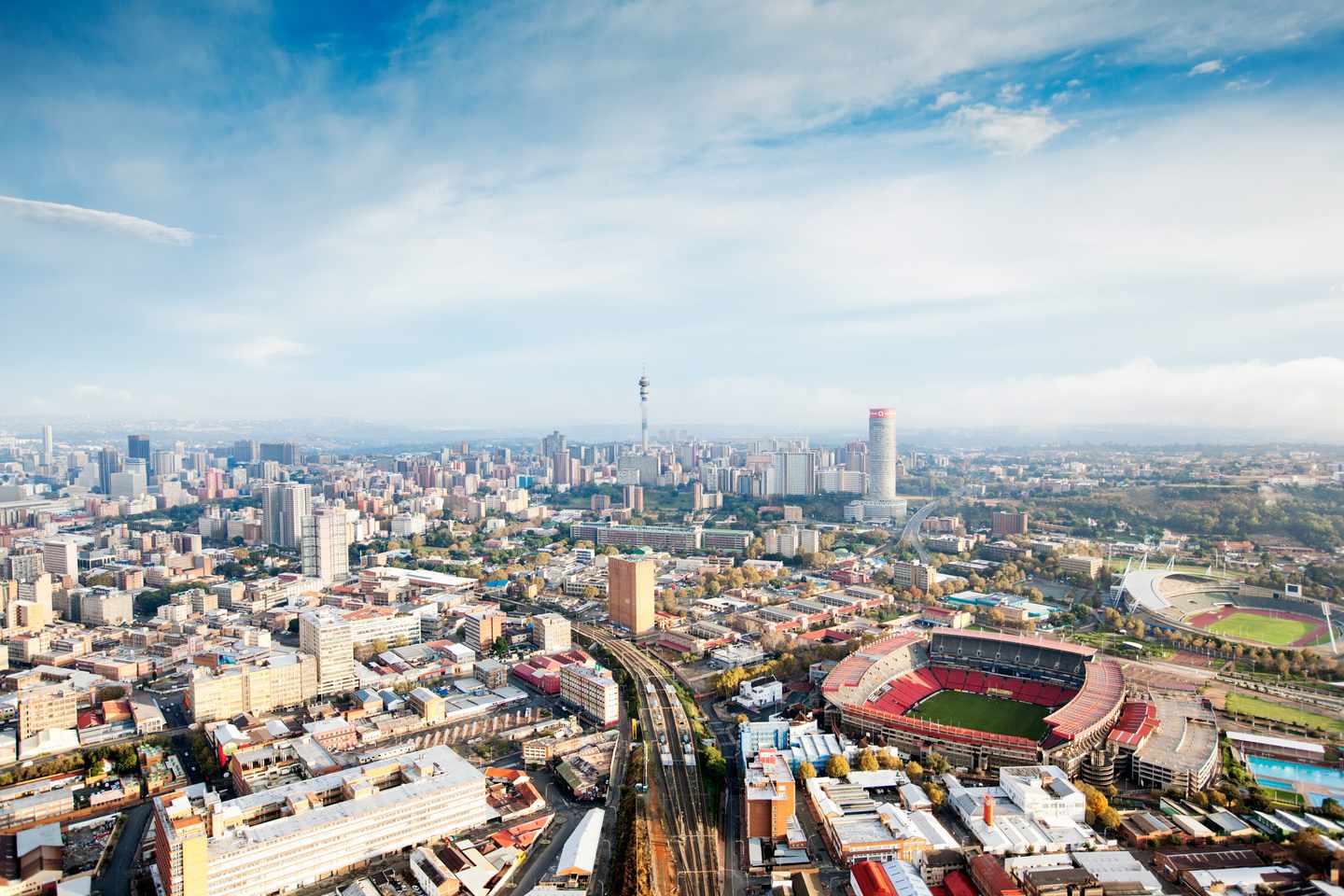 Luftaufnahme von Johannesburg mit dichter Bebauung, Hochhäusern, Bahntrassen und Stadion in Südafrika