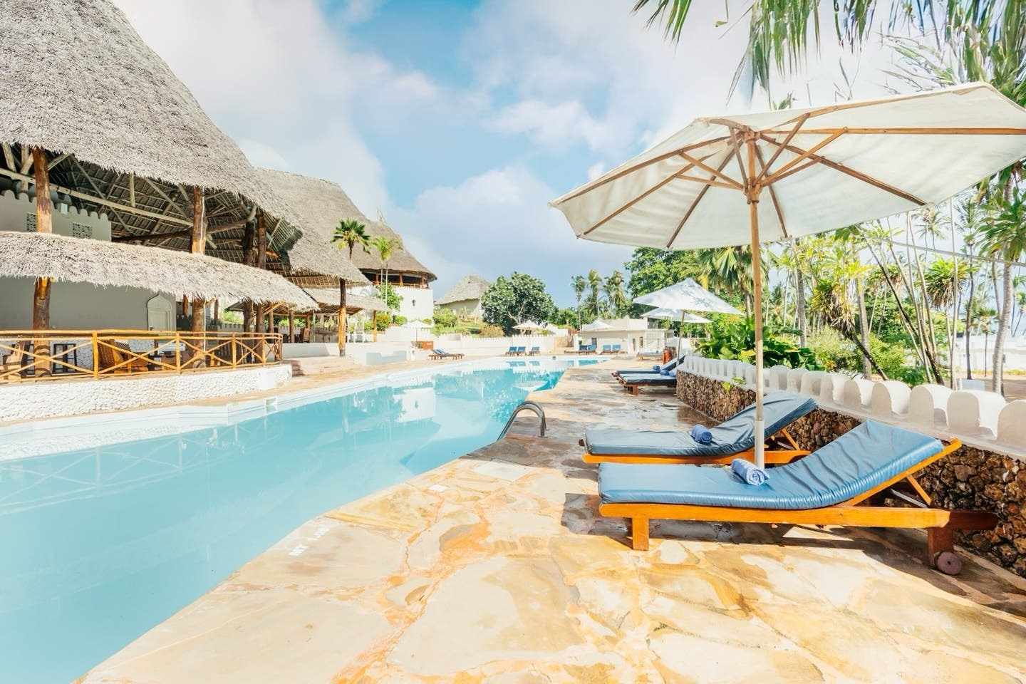 Poolbereich im ananea Diamonds Mapenzi Resort in Kiwengwa, Sansibar mit Sonnenliegen, Palmen und Makuti-Dächern in tropischer Umgebung
