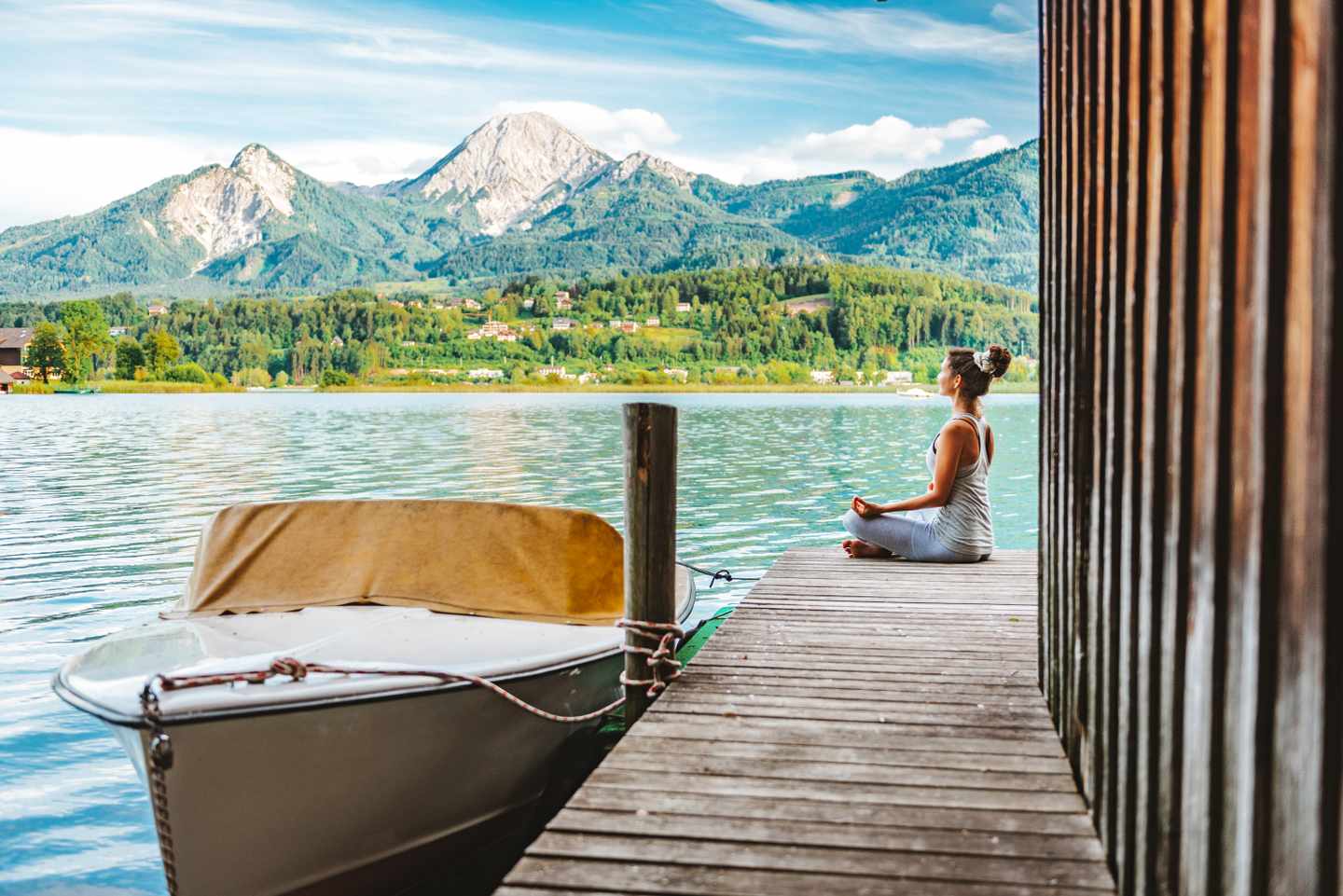 Alleinreisende meditiert auf einem Steg am Faaker See mit Blick auf die Berge der Karawanken