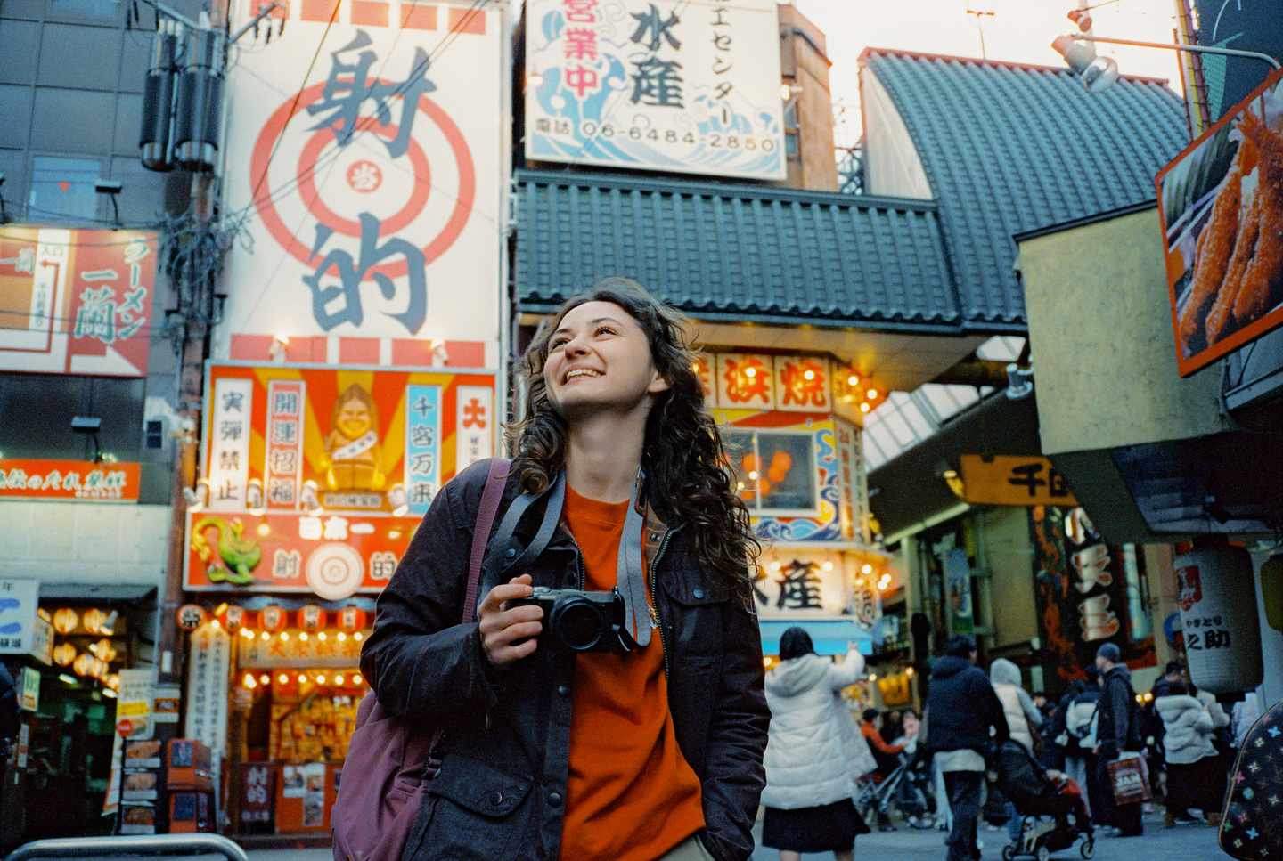 Alleinreisende Frau mit Kamera zwischen Restaurants und leuchtenden Schildern in Osaka