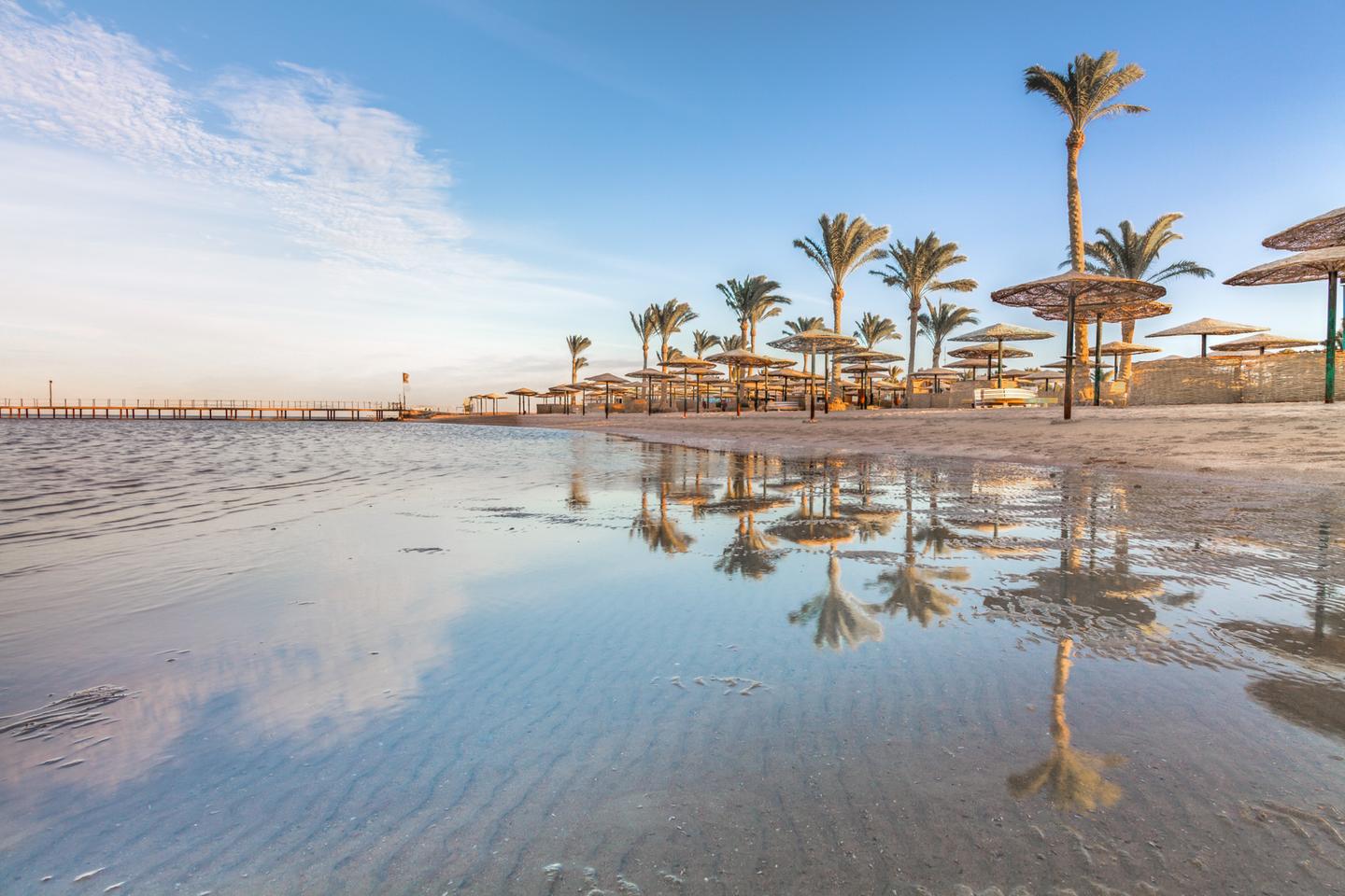 Sandstrand mit Palmen und Sonnenschirmen am Roten Meer während des Sonnenuntergangs in Ägypten
