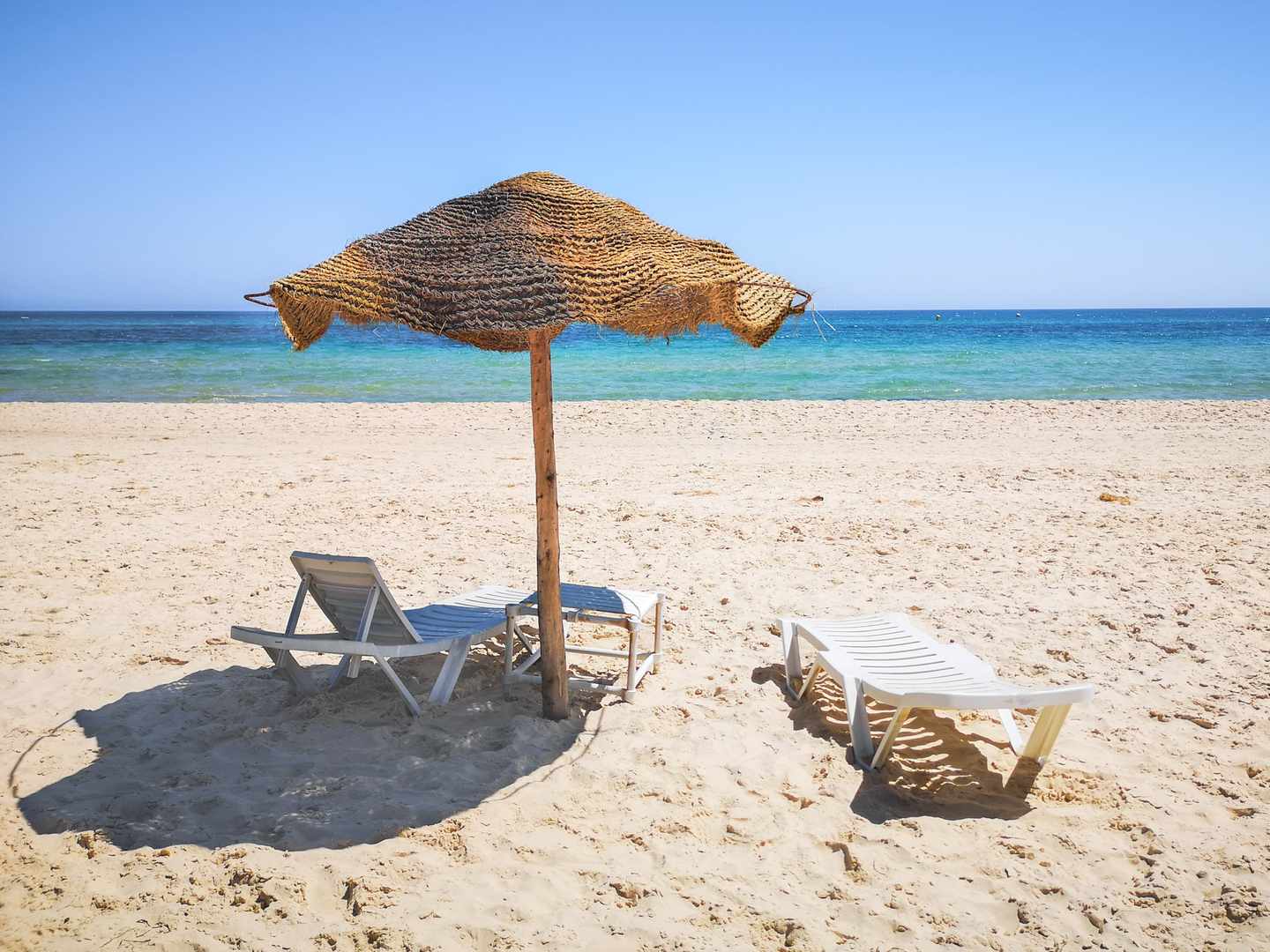 Sandstrand von Hammamet mit Strohschirm, Liegen und türkisblauem Mittelmeer an der tunesischen Küste