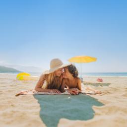 Mutter und Sohn liegen auf einem Strandtuch am Sandstrand und schauen sich lächelnd an