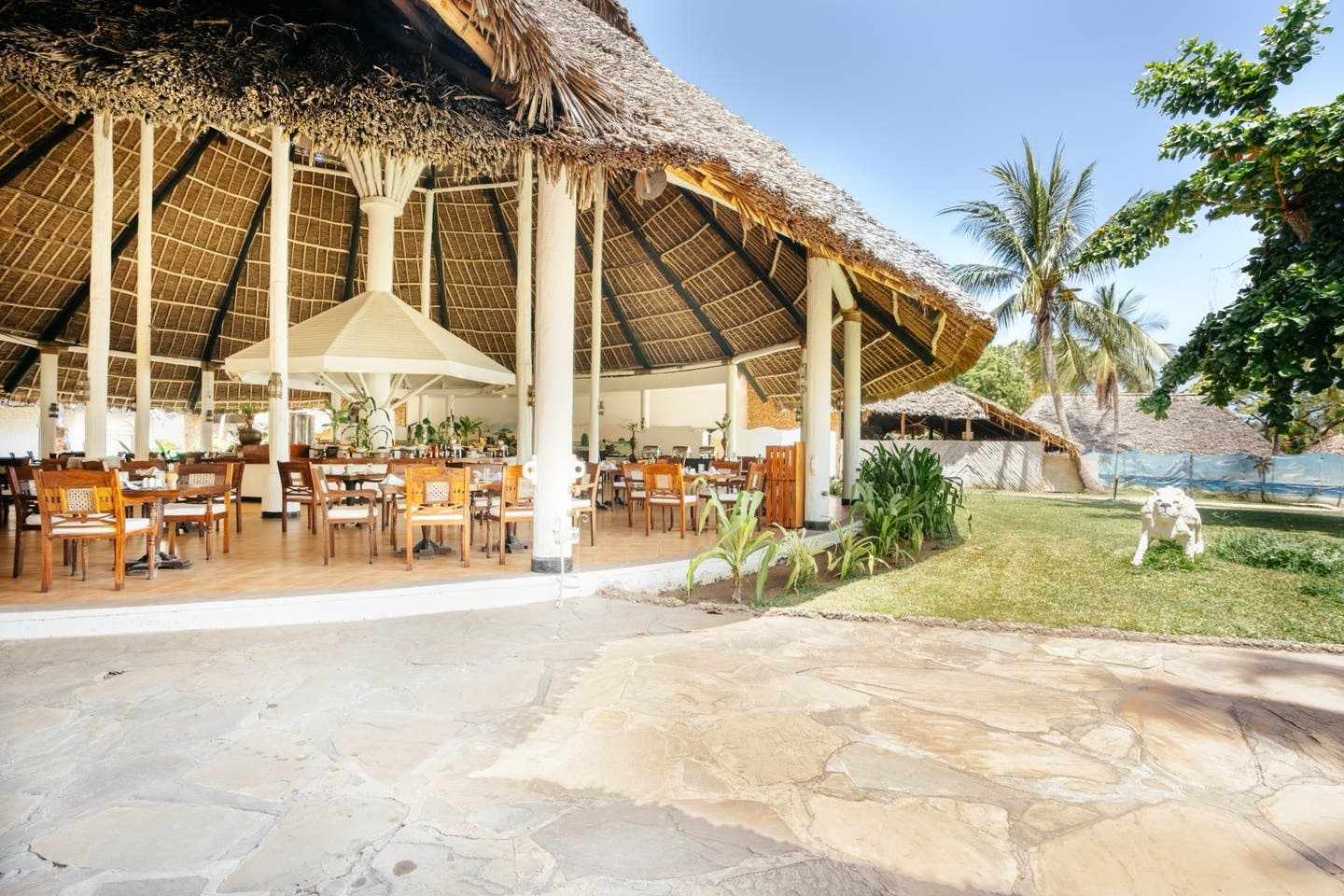 Offenes Restaurant im ananea Diamonds Malindi mit traditionellem Makuti-Dach, Holzmöbeln und tropischem Garten an Kenias Küste